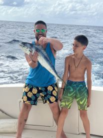 A young angler and an adult proudly displaying a large fish while aboard a boat in open waters.