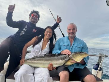 Three anglers celebrating a successful catch of a large fish while fishing offshore, showcasing their excitement on the boat.
