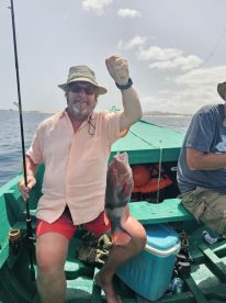 An angler proudly displaying a colorful Parrotfish while fishing from a small boat in a sunny coastal environment.