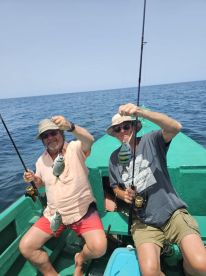 Two anglers proudly displaying their catch of colorful fish while fishing from a small boat in open waters.