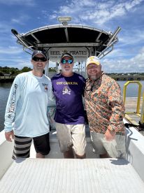 Three anglers posing on the deck of the 'Reel Pirates' boat, showcasing a sunny day on the water, perfect for fishing adventures.