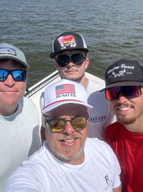 A group of four anglers enjoying a sunny day on the boat, showcasing camaraderie and excitement for fishing.