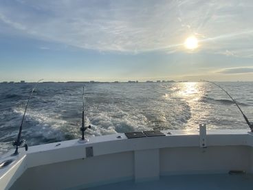 A scenic view from the back of a fishing boat, showcasing the ocean and distant skyline during a sunset cruise.