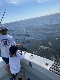 A young angler and an adult are actively reeling in a fish while fishing on a boat in open water, showcasing a thrilling moment on the Gulf Coast.