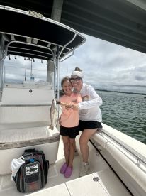 A young girl and her mother proudly displaying a caught fish on a boat, showcasing a fun family fishing experience.