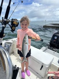 A young girl proudly displaying her catch, a silver fish, while fishing on a boat, showcasing a fun day on the water.