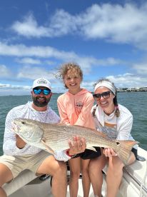 A family proudly displaying a large Redfish while enjoying a day on the water.
