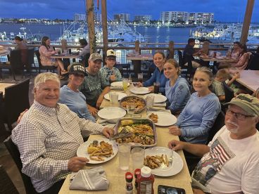 A family enjoying a meal at a restaurant with a view of the marina, showcasing a variety of dishes and a relaxed atmosphere.