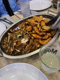 A platter of fried fish and seafood served at a dining table, with drinks and plates visible, suggesting a social dining experience.