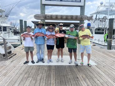 A family group proudly displaying their catch of Red Snapper at the marina after a successful fishing trip.