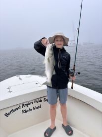 A young angler proudly displaying a striped bass while fishing on a foggy day in Rhode Island.