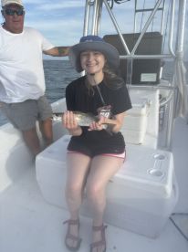 A smiling angler proudly displaying a caught Speckled Trout while aboard a fishing boat, with another person in the background.