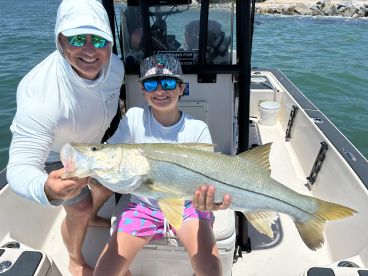 A young angler proudly displaying a large Snook while fishing on a boat, showcasing a sunny day on the water.
