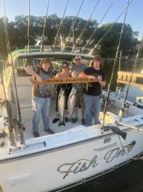 A group of four anglers proudly displaying their catch of two large fish on the boat 'Fish On' after a successful fishing trip.