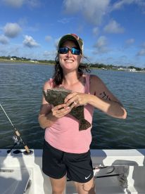Angler smiling while holding a large Flounder on a sunny day out on the water, showcasing a successful fishing trip.