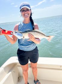 Angler proudly displaying a large Speckled Trout while fishing on a sunny day.