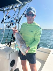 An angler proudly displaying a Redfish while aboard a fishing boat in a sunny coastal environment.