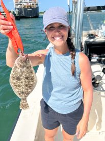 An enthusiastic angler proudly displaying a Flounder while fishing from a boat, showcasing a sunny day on the water.