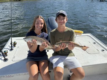 Two young anglers proudly displaying their catches of Speckled Trout while enjoying a sunny day on the water.