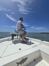 An angler actively fishing from a center console boat under a clear blue sky, showcasing a relaxed day on the water.