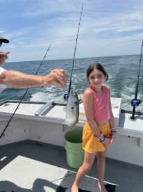 A young girl proudly poses with a small fish caught while fishing on a boat, showcasing a fun family fishing experience.