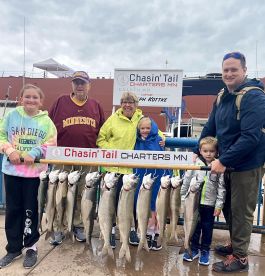 A family proudly displays their catch of Lake Trout on a catch board after a fishing trip with Chasin' Tail Charters in Duluth, MN.