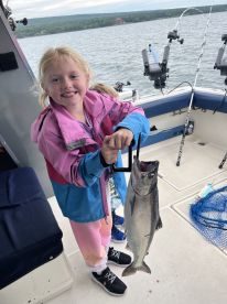 A young angler proudly displaying a freshly caught fish aboard a fishing boat, enjoying a day on the water.