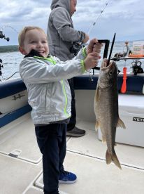 A young angler joyfully displaying a freshly caught fish while fishing on a boat, showcasing a fun family fishing experience.