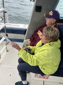 Two anglers engaged in fishing on a boat, with one actively holding a fishing rod while the other observes, showcasing a relaxed fishing experience.