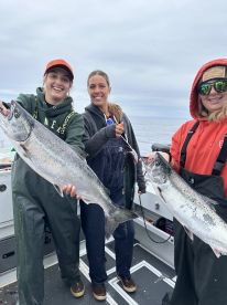 Three anglers proudly displaying their catch of salmon while fishing on a boat in open waters.