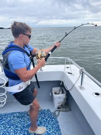 A young angler is actively reeling in a fish while fishing on a boat, showcasing the excitement of the catch in a coastal environment.