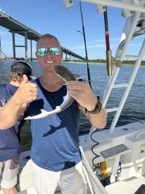 An angler proudly displaying a caught shark while fishing near a bridge, showcasing a sunny day on the water.