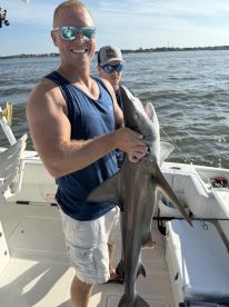 Angler proudly displaying a caught shark while fishing on a boat, showcasing a sunny day on the water.