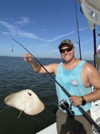 Angler proudly displaying a caught stingray while fishing on a sunny day in open waters.