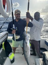 Two anglers proudly displaying a large Kingfish aboard a fishing boat, showcasing a successful deep-sea fishing trip.