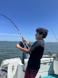 A young angler is actively reeling in a fish while fishing from a boat in a sunny coastal environment.