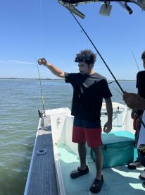 A young angler is actively reeling in a fish while fishing from a boat in a coastal environment.