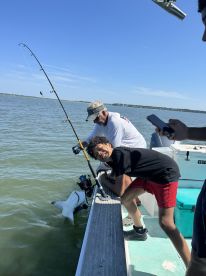 A young angler excitedly poses while reeling in a shark during a fishing trip, showcasing the thrill of the catch on a sunny day.
