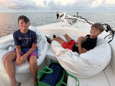 Two young anglers relaxing on bean bag seats inside a fishing boat, enjoying the calm waters during a fishing trip.