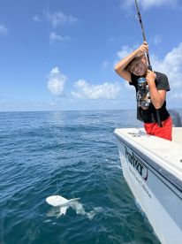 A young angler is reeling in a fish while fishing from a boat in clear blue waters, showcasing an exciting moment on the water.