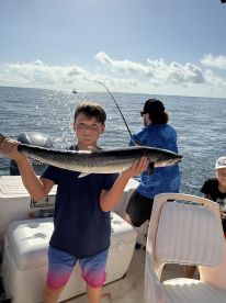 A young angler proudly displaying a large fish while fishing on a boat in sunny waters.