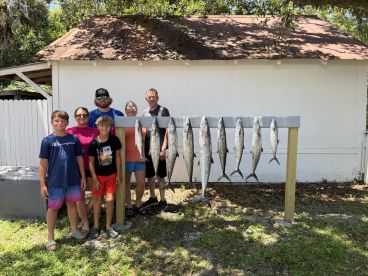 A family proudly displaying their catch of several Spanish Mackerel on a catch board after a successful fishing trip.