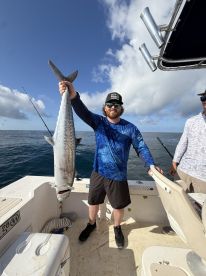 Angler proudly displaying a large King Mackerel aboard a fishing boat, enjoying a successful day on the water.