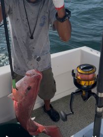 Angler reeling in a large Red Snapper while fishing on a boat, showcasing the excitement of the catch.