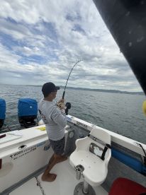 An angler reeling in a catch while fishing from a boat, surrounded by a scenic ocean backdrop.