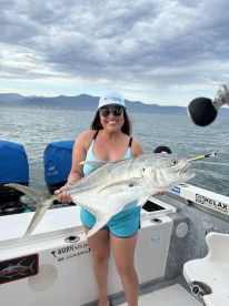 A proud angler displaying a large Jack Crevalle while fishing on a boat, surrounded by a scenic coastal backdrop.