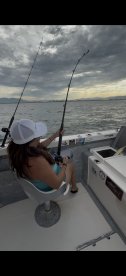 A female angler is actively fishing from a boat, showcasing the excitement of reeling in a catch against a scenic backdrop.
