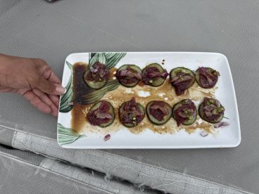 A hand presenting a plate of sushi-style cucumber bites topped with fish, likely prepared from a recent catch.