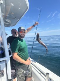 Angler reeling in a catch while fishing on a boat in open waters, showcasing a lively fishing experience.