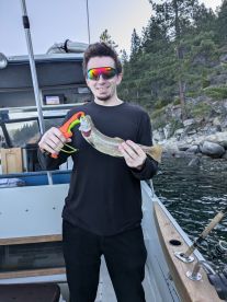 Angler proudly displaying a Rainbow Trout while fishing from a boat in a scenic lake environment.